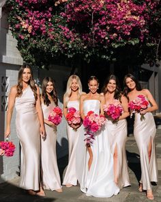 a group of women standing next to each other holding bouquets in front of a building