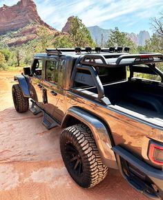 a truck parked on the side of a dirt road in front of some mountains and trees