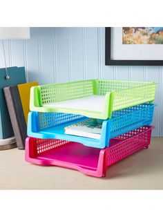 three colorful plastic baskets stacked on top of each other in front of a painting and lamp