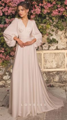 a woman standing in front of a flower covered wall wearing a long white dress with puff sleeves