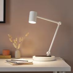 a white lamp sitting on top of a desk next to a vase with flowers in it