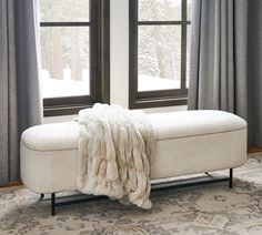 a white bench sitting in front of two windows covered with blankets and fur on top of it