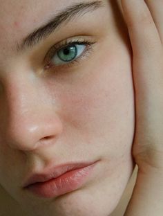 a close up of a woman's face with her hand on her head and blue eyes