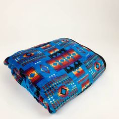 a blue blanket with an orange and red design is folded up on a white surface