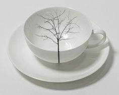 a white cup and saucer with a tree painted on it