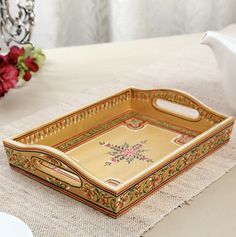 an ornately decorated tray sits on a table next to a white teapot and red flowers