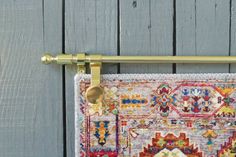 a close up of a rug hanging on a metal rod with a wooden wall in the background