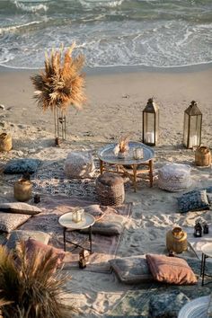 an outdoor seating area is set up on the beach with candles, pillows and rugs