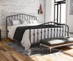 a bedroom with white brick walls and black iron bed frame, footstools, pillows, and rugs