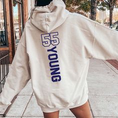 a woman walking down the street wearing a white hoodie with blue letters on it