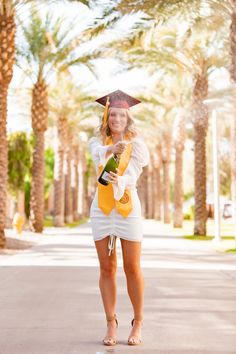 a woman in a graduation gown holding a bottle of wine and posing for the camera