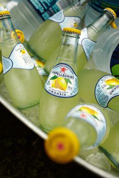 several bottles of lemonade sitting on top of a metal tray filled with water and lemons