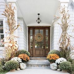 the front door is decorated with fall flowers and pumpkins for display on either side