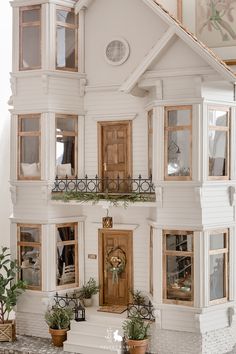 a doll house with potted plants in front of the door and windows on the second floor