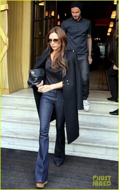 a woman in black coat and jeans walking out of a building with a man standing behind her