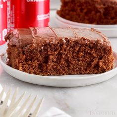 a slice of chocolate cake on a plate with a can of coke in the background