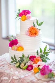 a three tiered white cake with colorful flowers on top and greenery around it