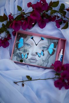 a pink frame with blue butterflies on it next to red flowers and a white sheet