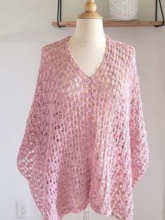 a pink crocheted sweater on a mannequin stand next to a white wall