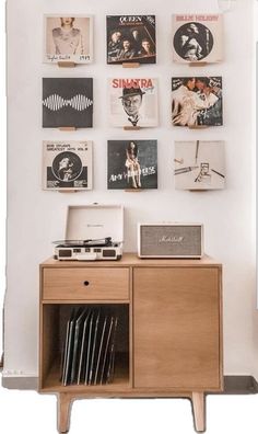 a record player sitting on top of a wooden cabinet in front of a wall covered with records