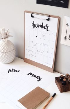 a desk with a calendar, pen and some other items on it next to a pineapple