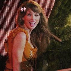 a woman with her tongue out standing in front of a screen wearing a yellow dress