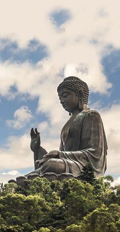 a large buddha statue sitting on top of a lush green field under a blue cloudy sky