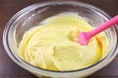 a glass bowl filled with yellow batter and a pink spoon in the middle, on a wooden table