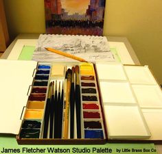 an artist's palette with watercolors and brushes on it, next to a painting