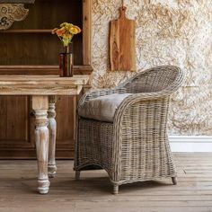 a wicker chair sitting in front of a wooden table with a vase on it