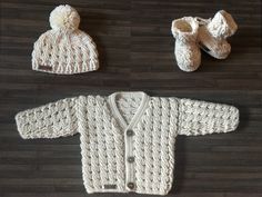 two knitted baby sweaters and booties are laid out on a wood floor