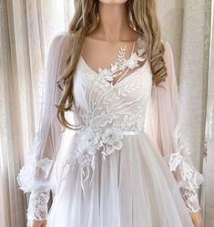 a mannequin wearing a white wedding dress with sheer sleeves and floral appliques