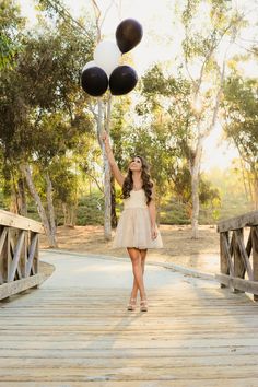 a woman in a dress holding two black and white balloons while walking across a bridge