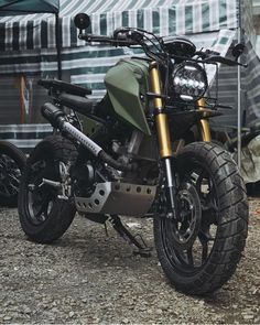 a green motorcycle parked on top of a gravel road next to a trailer with a tent in the background