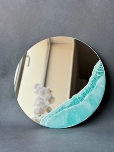 a round mirror on the wall above a vase with white flowers and a door in the background