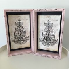 two framed pictures with chandelier designs in pink and black frames on a white table