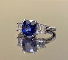 "DeKara Designs Collection Beautiful Modern/Art Deco Ceylon Blue Sapphire and Diamond Ring Metal- 90% Platinum, 10% Iridium Stones- Genuine Cushion Cut Ceylon/Sri Lanka Royal Blue Sapphire 2.87 Carats. Two Trapezoid Cut Diamonds G-H Color VS1 Clarity 0.93 Carats. Size-6. FREE SIZING Entirely Handmade, Classic and Timeless Art Deco Inspired Ceylon Cushion Cut Royal Blue Sapphire Diamond Engagement Ring. This ring is out of this world with the center Ceylon Sapphire being exceptional in quality, c Blue Three Stone Platinum Jewelry, Elegant Blue Sapphire Three Stone Ring, Platinum Blue Three Stone Rings, Blue Three-stone Cushion-cut Jewelry, Blue Three-stone Cushion Cut Jewelry, Gia Certified Blue Baguette Cut Sapphire Ring, Luxury Royal Blue Sapphire Ring For Wedding, Blue Three Stone Cushion Cut Jewelry, Gia Certified Blue Jewelry For Wedding