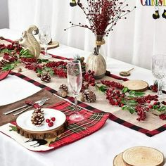 the table is set for christmas dinner with red berries and pine cones