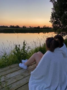 two people sitting on a bench looking out over the water at sunset, with one person wrapped in a towel