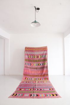 a pink blanket sitting on top of a white floor next to a light hanging from the ceiling