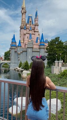 a woman standing on a bridge looking at the castle in front of her is wearing minnie mouse ears