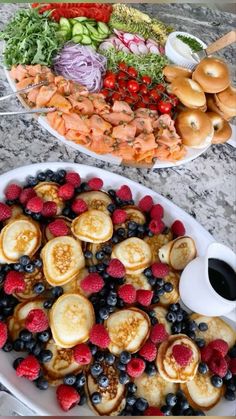 two plates filled with pancakes and fruit on top of a table next to a platter of food