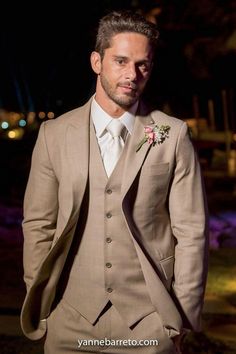 a man in a tan suit and flower boutonniere is looking at the camera