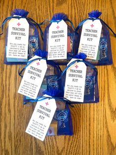 six teacher survival kit bags on a wooden table with blue ribbon and tags attached to them