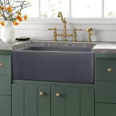 a kitchen sink with green cabinets and gold faucets on the countertop next to a window