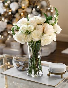 a glass vase with white flowers on a table in front of a decorated christmas tree