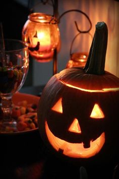 a carved pumpkin sitting on top of a table next to some wine glasses and candles