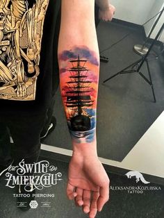 a man's arm with a ship on it and the sun setting in the background