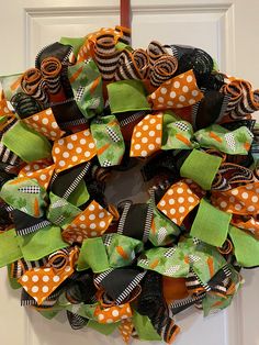 a wreath with orange, black and green bows hanging on the front door for halloween