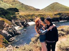 a man and woman standing next to each other in front of a body of water